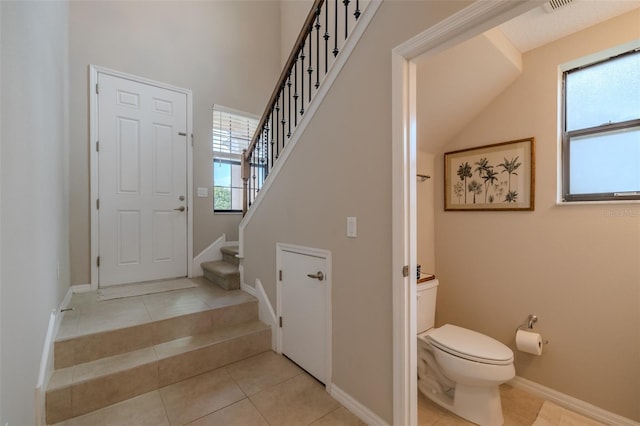 bathroom featuring toilet, tile patterned floors, baseboards, and a high ceiling