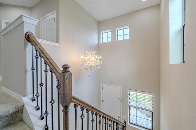 stairs with an inviting chandelier, carpet, a towering ceiling, and a healthy amount of sunlight