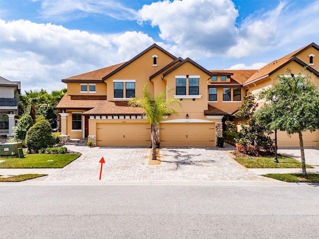 view of property featuring a garage, stucco siding, decorative driveway, and stone siding