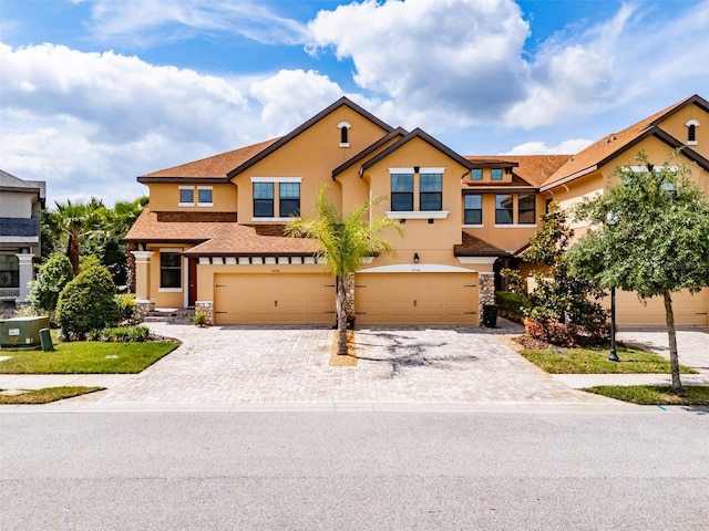 multi unit property featuring decorative driveway, a garage, stucco siding, and stone siding