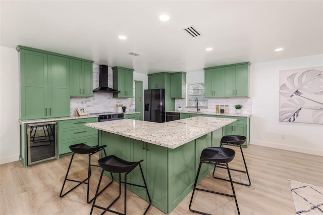 kitchen with wall chimney range hood, a breakfast bar area, a kitchen island, visible vents, and black appliances