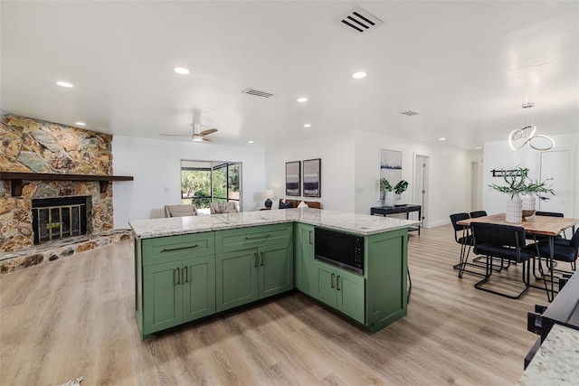 kitchen with visible vents, black microwave, light wood-style floors, a stone fireplace, and green cabinets