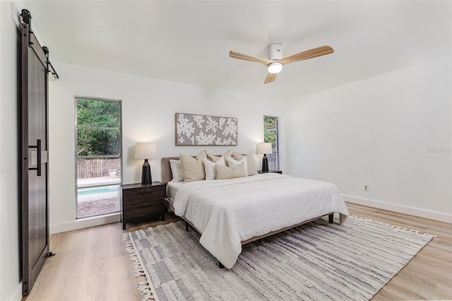 bedroom featuring baseboards, a barn door, ceiling fan, and light wood-style floors