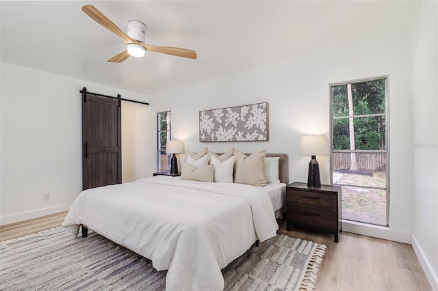 bedroom featuring baseboards, ceiling fan, light wood finished floors, and a barn door
