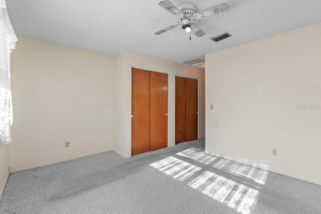 unfurnished bedroom with two closets, a ceiling fan, visible vents, and carpet