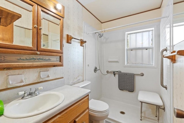 bathroom with vanity, a tile shower, toilet, and wallpapered walls