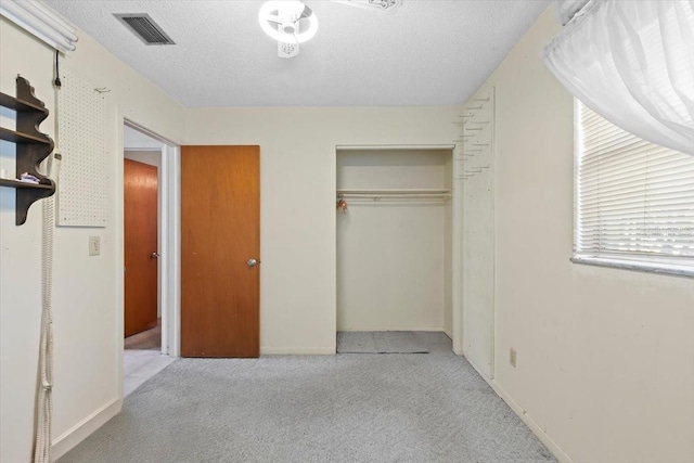 unfurnished bedroom with a textured ceiling, carpet, baseboards, visible vents, and a closet