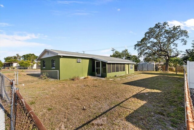 back of house featuring a sunroom, a fenced backyard, a lawn, and stucco siding