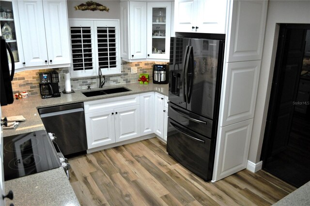 kitchen featuring backsplash, light wood-type flooring, dishwasher, a sink, and black refrigerator with ice dispenser
