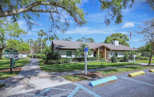 view of front of home featuring a front lawn, uncovered parking, stucco siding, and a chimney