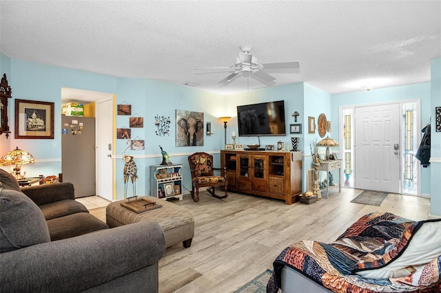 living room featuring light wood-type flooring, a ceiling fan, and a textured ceiling