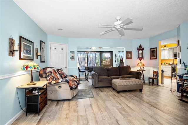 living area with baseboards, a textured ceiling, light wood finished floors, and ceiling fan