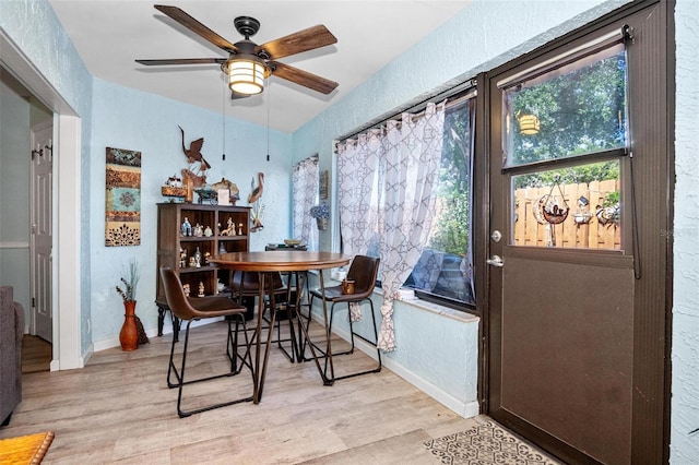 dining room with ceiling fan, a textured wall, baseboards, and light wood-style floors