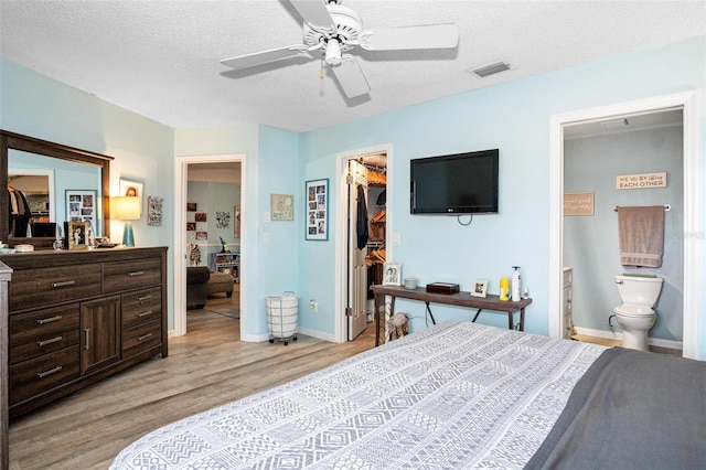 bedroom featuring a walk in closet, a textured ceiling, light wood-style flooring, visible vents, and a closet