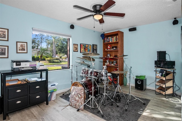recreation room featuring a ceiling fan, a textured ceiling, baseboards, and light wood-style floors