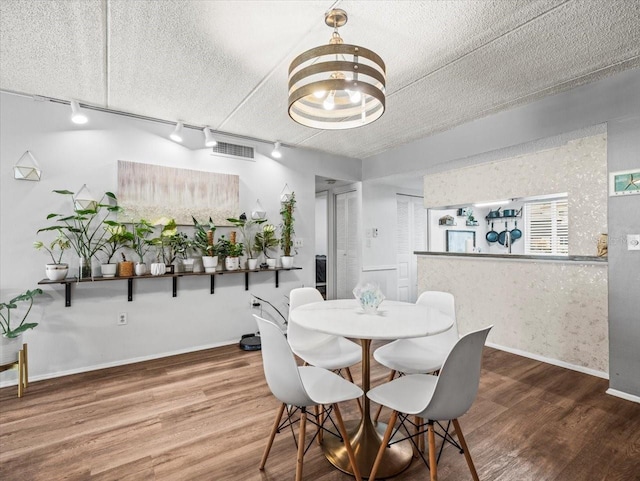 dining area with an inviting chandelier, track lighting, baseboards, wood finished floors, and visible vents