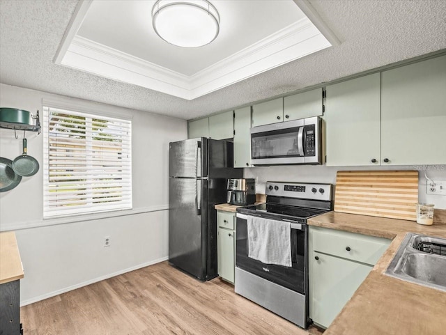 kitchen featuring crown molding, appliances with stainless steel finishes, a sink, light wood finished floors, and light countertops