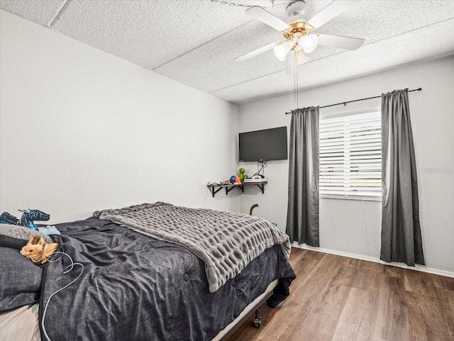 bedroom with a textured ceiling, baseboards, ceiling fan, and wood finished floors