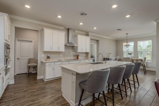 21590 Violet Periwinkle Dr, Land O Lakes, FL 34637 - kitchen with white cabinets, a sink, a kitchen island with sink, a breakfast bar area, and wall chimney exhaust hood