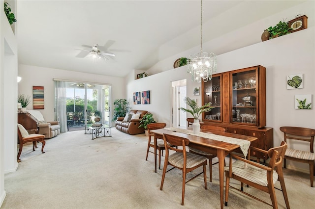 dining space with ceiling fan with notable chandelier, light colored carpet, and vaulted ceiling