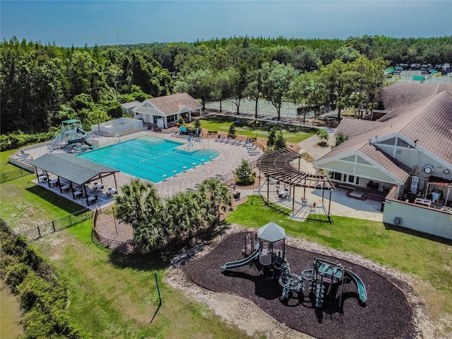 community pool with a patio, a view of trees, fence, and a lawn