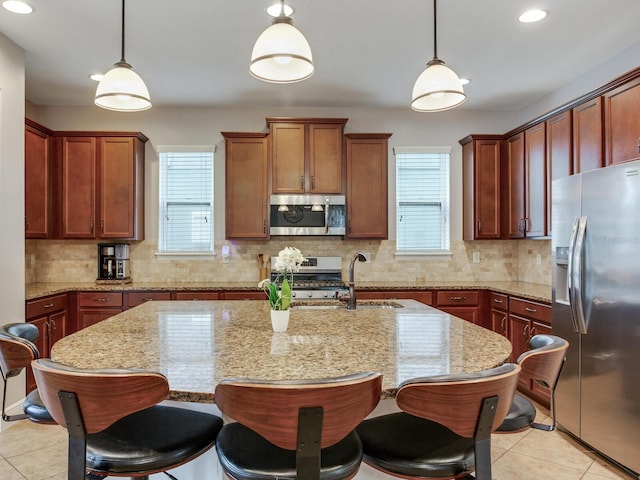 kitchen featuring appliances with stainless steel finishes, plenty of natural light, light tile patterned flooring, and an island with sink