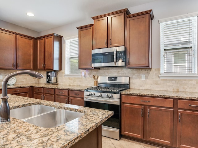 kitchen with light tile patterned flooring, light stone countertops, a sink, stainless steel appliances, and tasteful backsplash