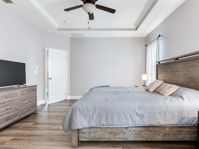 bedroom featuring a raised ceiling, baseboards, wood finished floors, visible vents, and ornamental molding