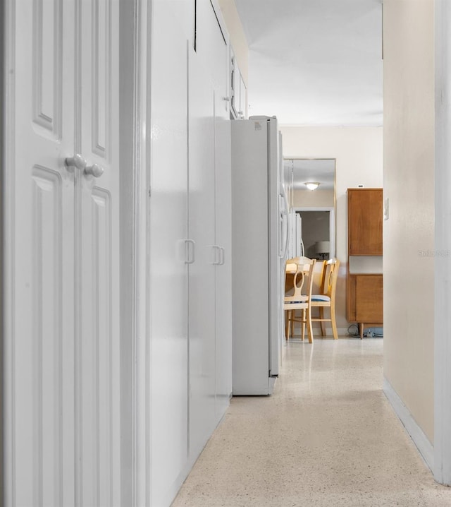 hall featuring baseboards and light speckled floor