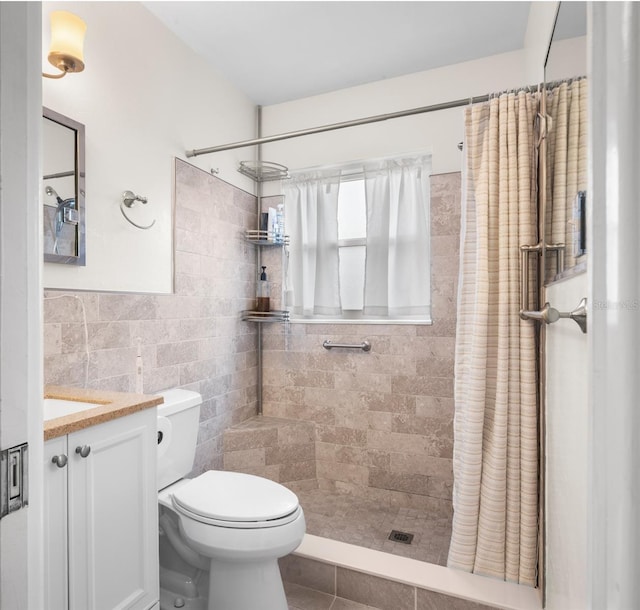 bathroom with a tile shower, vanity, toilet, tile patterned floors, and tile walls