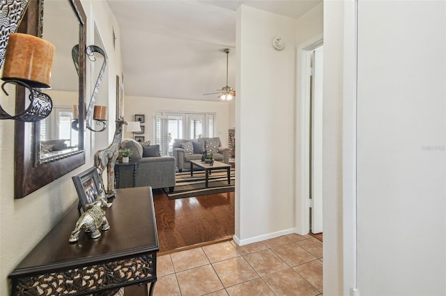 corridor featuring baseboards, lofted ceiling, and light tile patterned floors