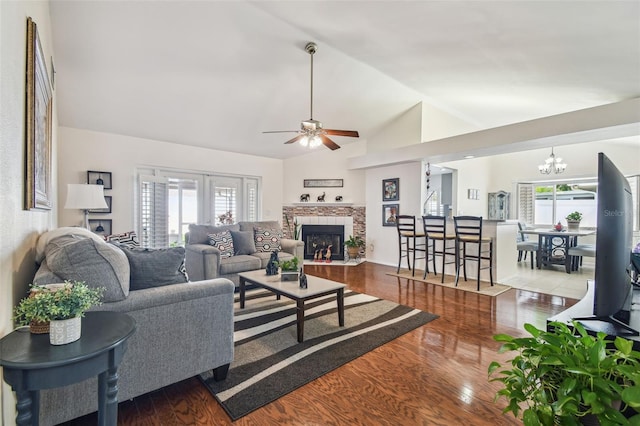 living room with ceiling fan with notable chandelier, wood finished floors, vaulted ceiling, and a wealth of natural light