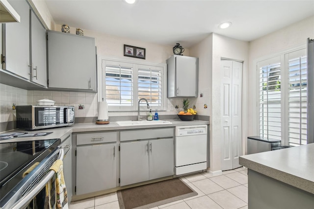 kitchen featuring a sink, gray cabinets, stainless steel appliances, light tile patterned floors, and tasteful backsplash