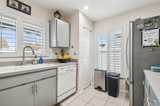 kitchen with freestanding refrigerator, light tile patterned flooring, white dishwasher, light countertops, and a sink