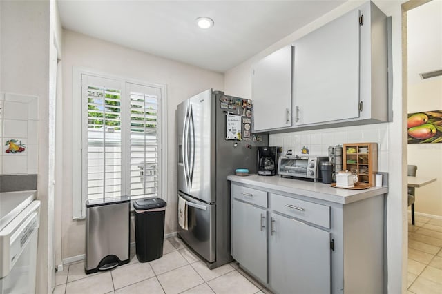kitchen with stainless steel refrigerator with ice dispenser, light countertops, gray cabinets, light tile patterned floors, and backsplash