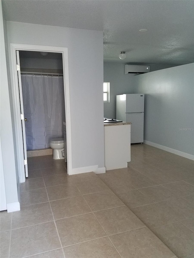 interior space featuring tile patterned flooring, a wall mounted air conditioner, baseboards, and a textured ceiling