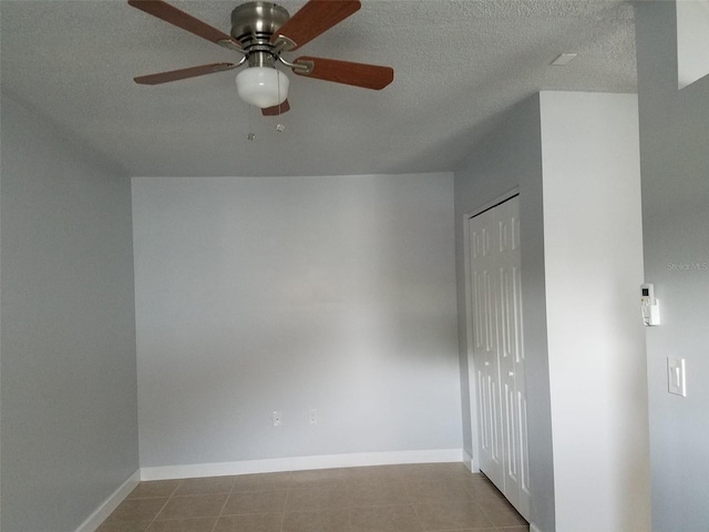 empty room featuring a textured ceiling, ceiling fan, baseboards, and tile patterned flooring