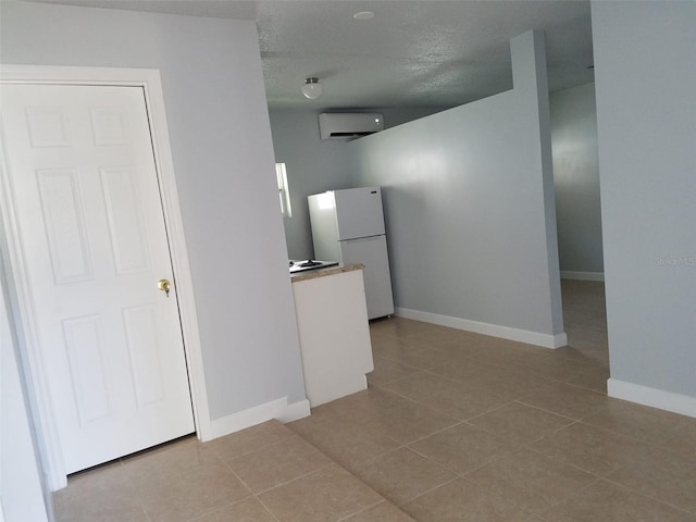 kitchen featuring an AC wall unit, freestanding refrigerator, baseboards, and tile patterned flooring