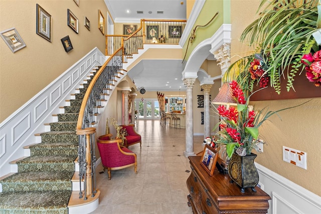 entryway featuring decorative columns, a towering ceiling, arched walkways, ornamental molding, and stairs