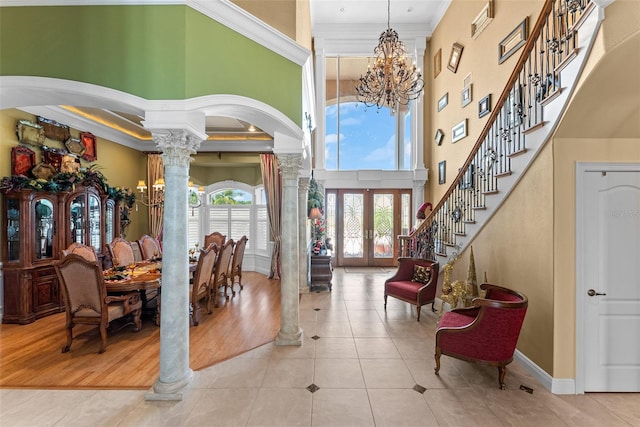 tiled foyer entrance with an inviting chandelier, ornamental molding, a high ceiling, ornate columns, and arched walkways