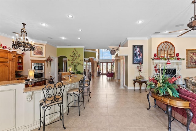 kitchen with stainless steel double oven, a kitchen bar, crown molding, arched walkways, and ceiling fan with notable chandelier