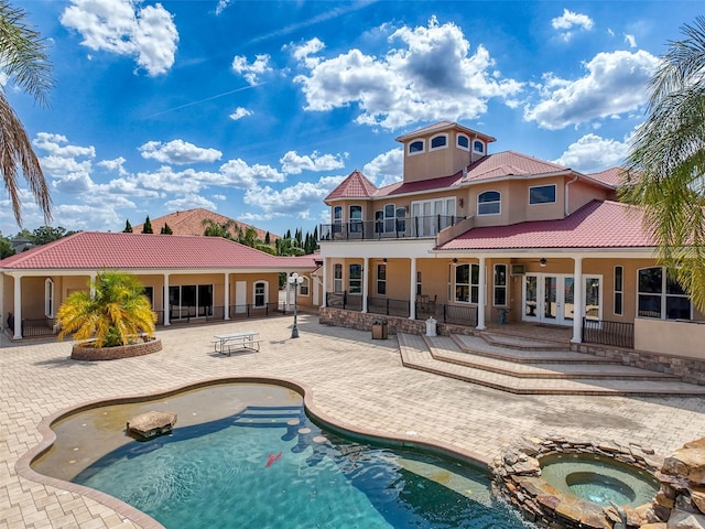 rear view of property featuring an in ground hot tub, a tile roof, a patio area, a balcony, and stucco siding
