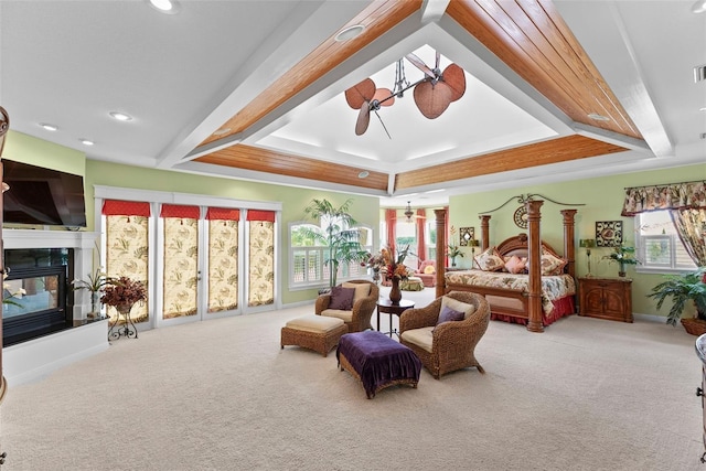 carpeted bedroom with baseboards, a glass covered fireplace, a tray ceiling, and multiple windows