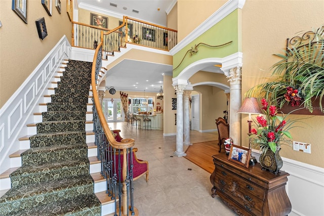 stairs with tile patterned flooring, ornamental molding, a high ceiling, ornate columns, and arched walkways