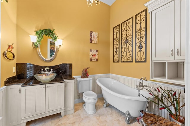 bathroom with toilet, a freestanding bath, wainscoting, and vanity