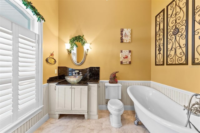 full bath featuring vanity, wainscoting, a freestanding bath, and toilet