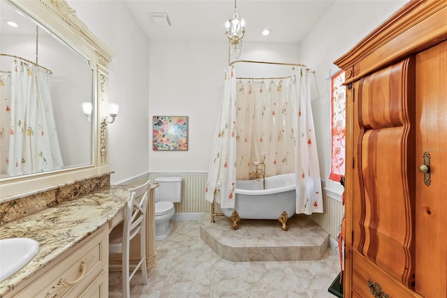 bathroom featuring wainscoting, vanity, toilet, visible vents, and a soaking tub