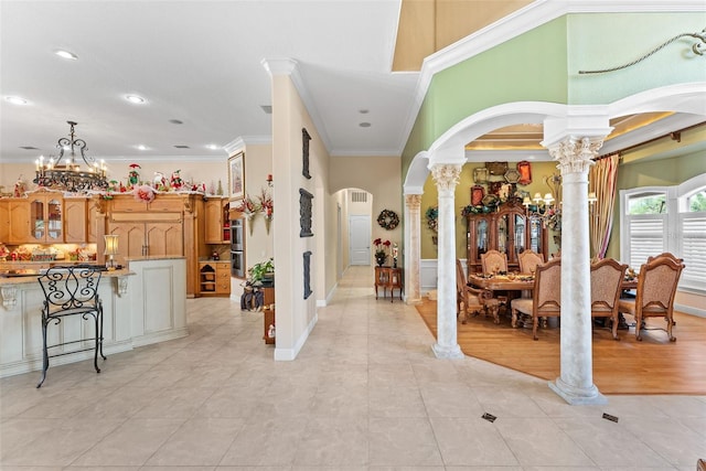 entrance foyer with an inviting chandelier, arched walkways, decorative columns, light tile patterned floors, and ornamental molding