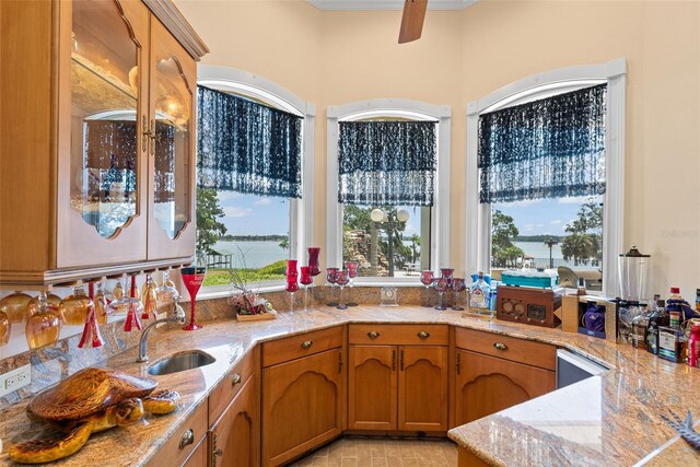 kitchen with crown molding, ceiling fan, light stone countertops, a sink, and brown cabinetry