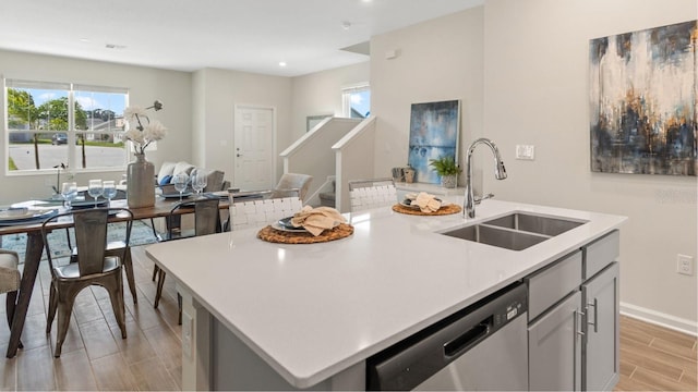 kitchen with plenty of natural light, stainless steel dishwasher, wood finish floors, a sink, and light countertops